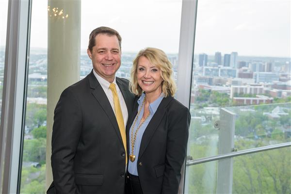 Dr. Gilliam and Debbie Gilliam smile at the camera while standing in front of a window. Behind them, the Birmingham skyline can be seen.